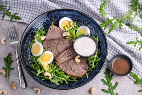 A plate of sliced beef with egg, rocket and cashew nuts, KETO program